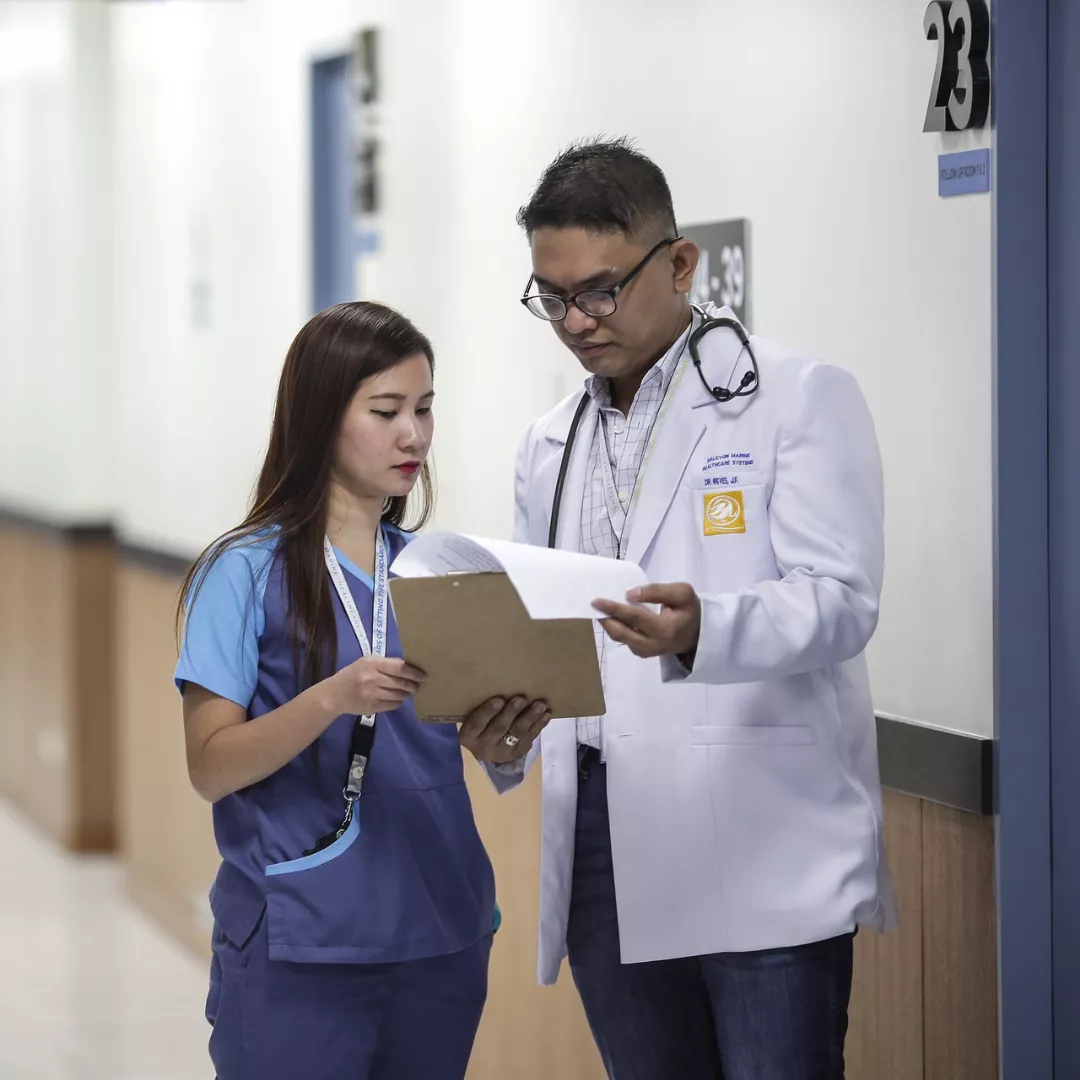 Two health practitioners looking over medical notes inside a hospital hallway